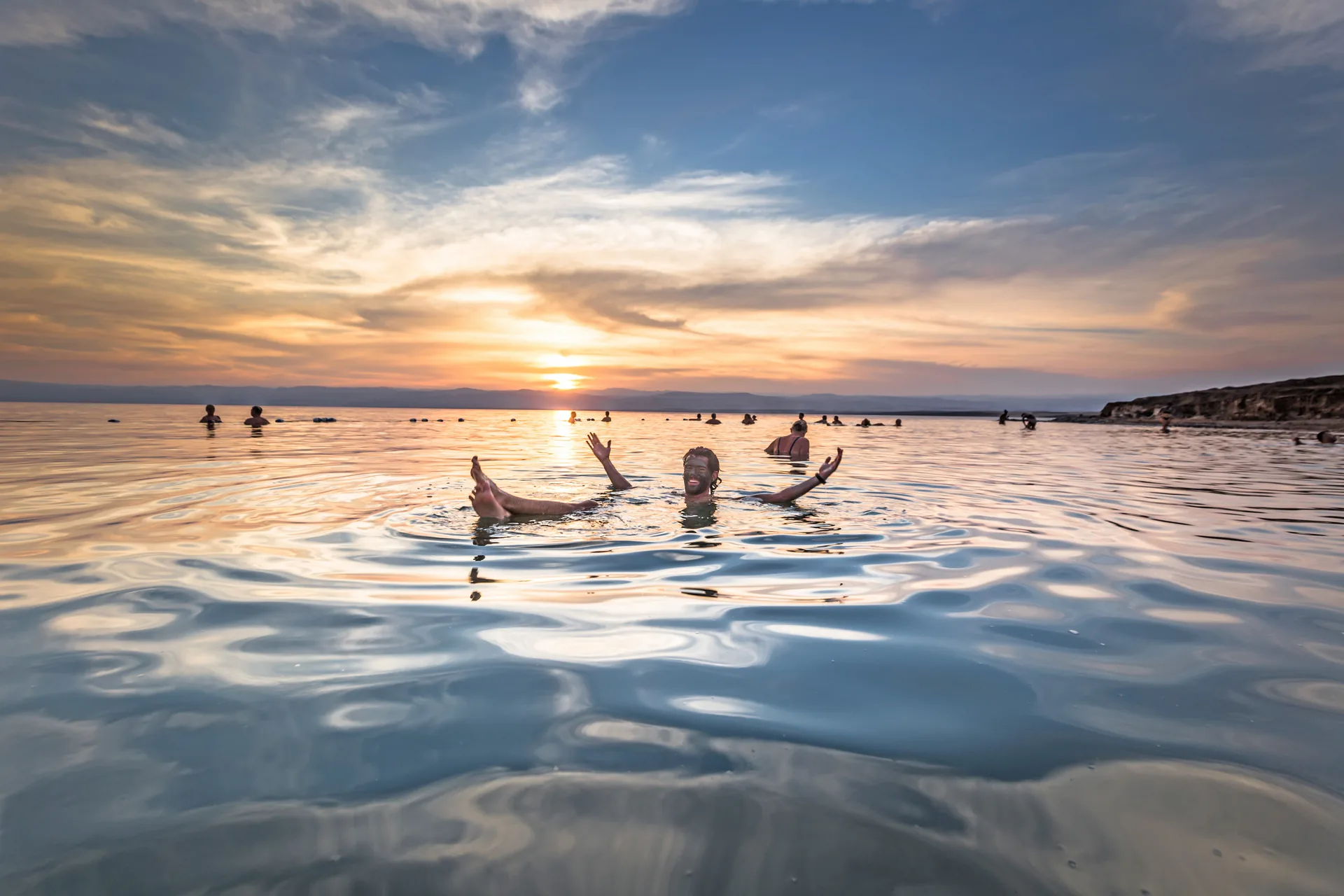 Visitors floating in the Dead Sea at sunset in Jordan